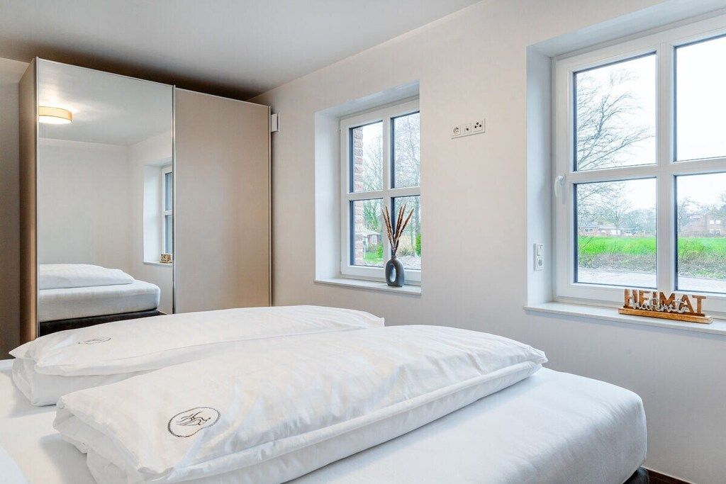 Une chambre d’hôtel avec deux lits, un grand miroir, une fenêtre donnant sur un beau paysage et une petite table sur laquelle est posé un vase.