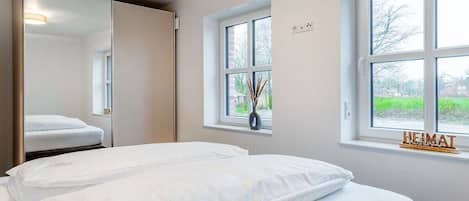 Habitación de hotel con dos camas, un espejo grande, una ventana con vistas y una pequeña mesa con un florero.