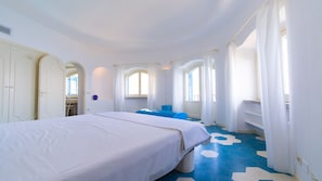 Una habitación de hotel con una cama, un banco azul y un ventanal con cortinas.