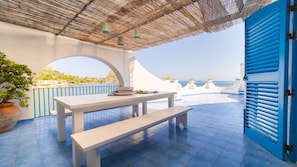 Una terraza con una mesa y bancos, con vistas a la costa.