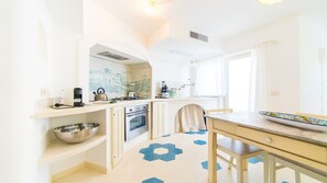 Een compacte keuken met witte kastjes, een gasfornuis, een inbouwoven en een eethoek met een tafel en stoelen.