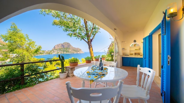 Un balcón con una mesa y sillas, que ofrece vistas panorámicas del mar y una montaña.