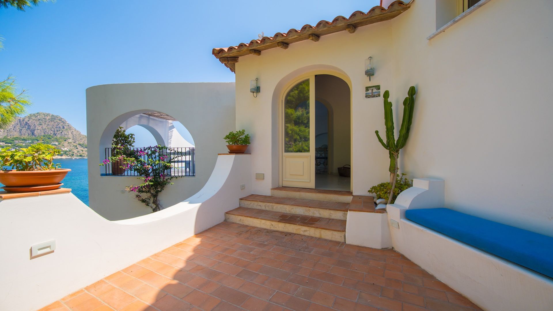 A Mediterranean-style building with a tiled patio, a small archway, and a view of the sea.