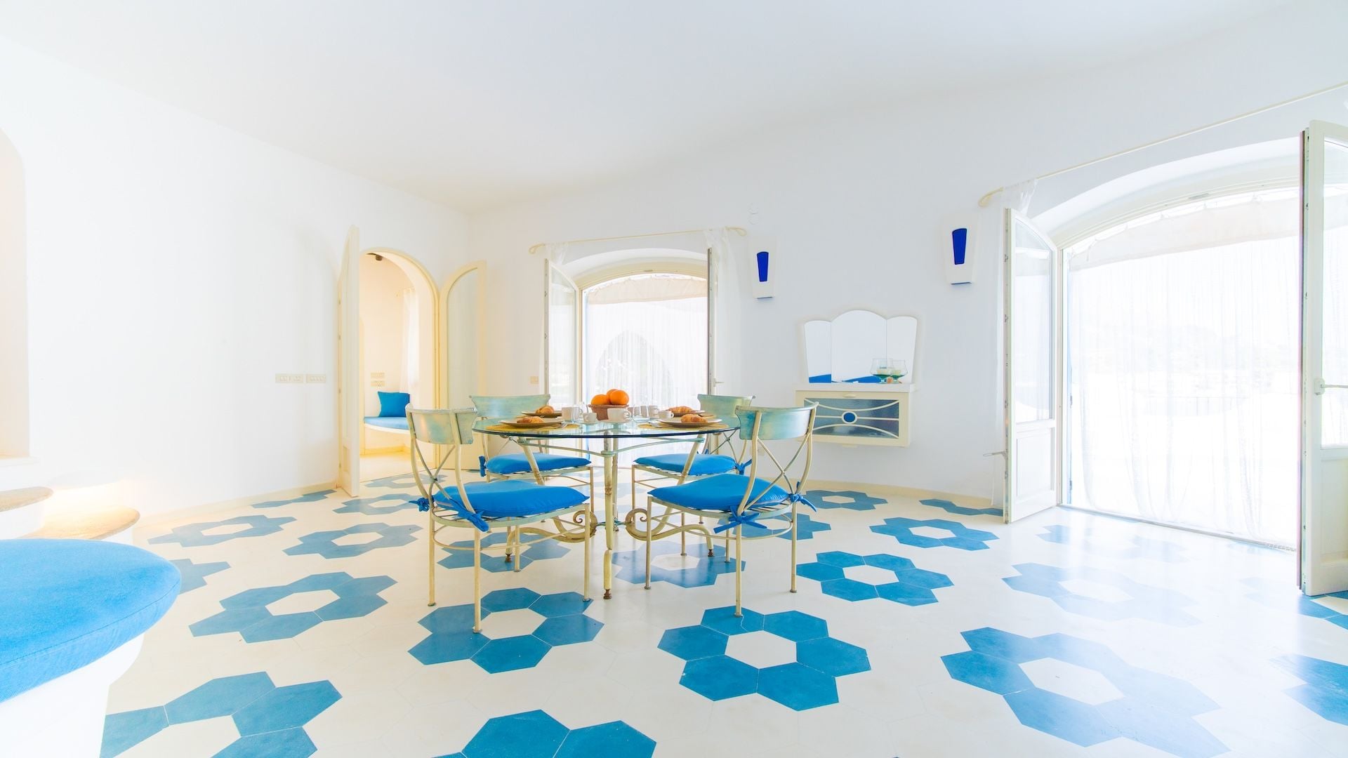 Een lichte kamer met een ronde glazen tafel, blauwe stoelen en een vloer met een patroon.