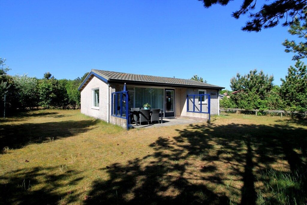 A small house with a single door and window, a patio with a table and chairs, and a fenced yard.