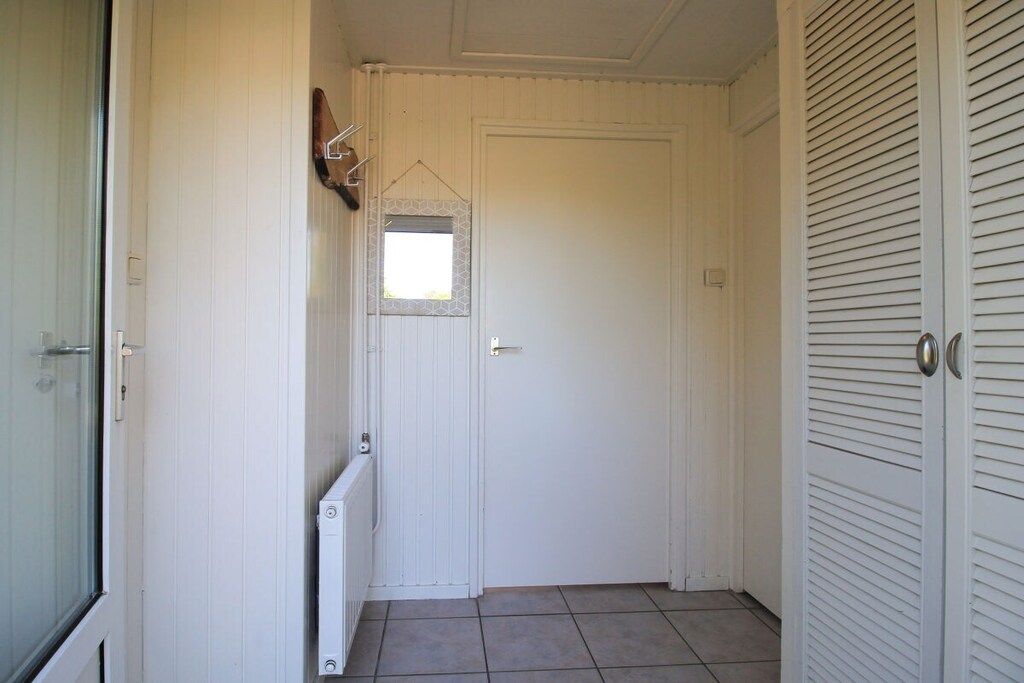 Un couloir avec une porte fermée, un radiateur et une petite fenêtre.