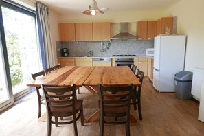 A modern kitchen with wooden cabinets, a large wooden dining table, and a view through the window. - Holiday home with 2 bedrooms (Hollum Ameland)