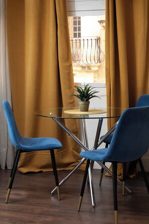 Un coin repas avec une table en verre, deux chaises bleues et une plante en pot.