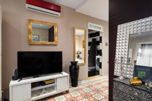 Una sala de estar con un televisor de pantalla plana, un espejo grande y un aire acondicionado instalado en la pared.