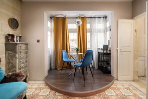 Una habitación con una mesa redonda de madera, dos sillas azules, una pequeña planta en maceta y un aparador decorativo.