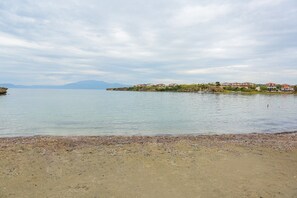 A coastal landscape with a sandy beach, calm water, and a distant shoreline with buildings. - Beachfront Big Villa (Çeşme)