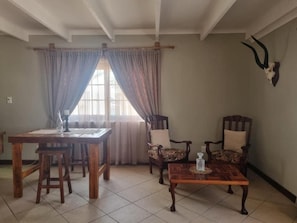 Un coin repas avec une table et des chaises en bois, une fenêtre avec des rideaux et un crâne d’animal accroché au mur.
