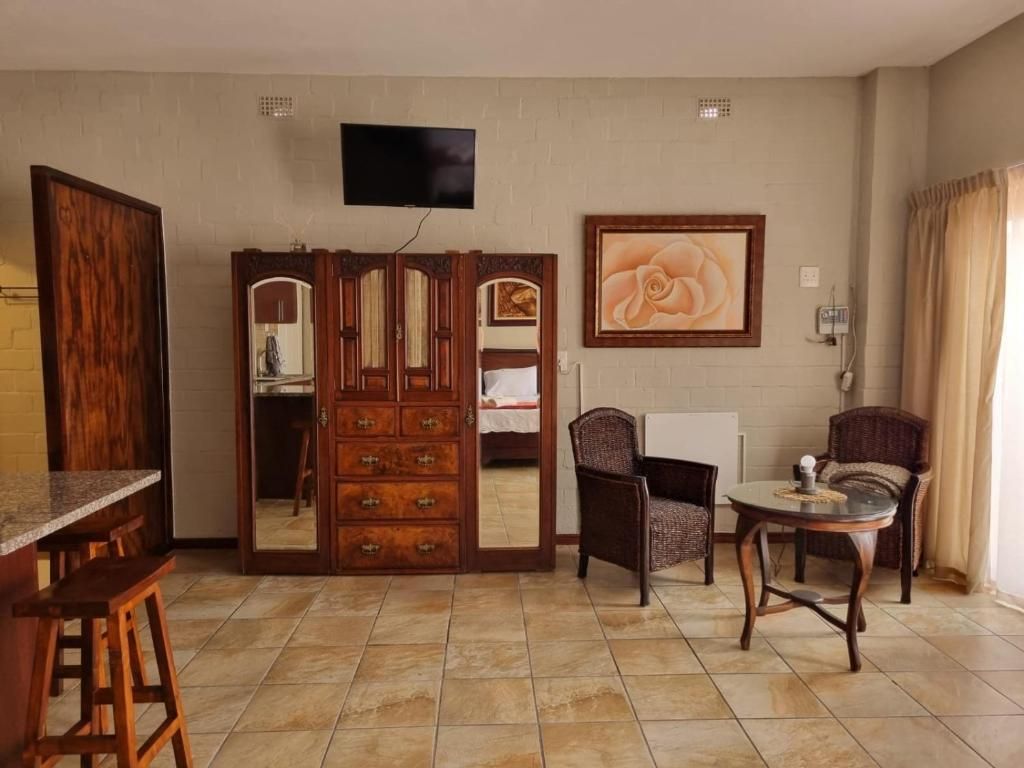 Una habitación con un armario de madera, un televisor montado en la pared, un cuadro enmarcado y una mesa de comedor con sillas.