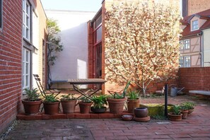 A courtyard with a brick wall, a wooden table, and potted plants. - Holiday apartment in Tangermünde with Wi-Fi (Tangermünde)