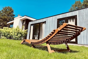 Ein modernes Haus mit einem großen Fenster und einem Holzliegenstuhl.