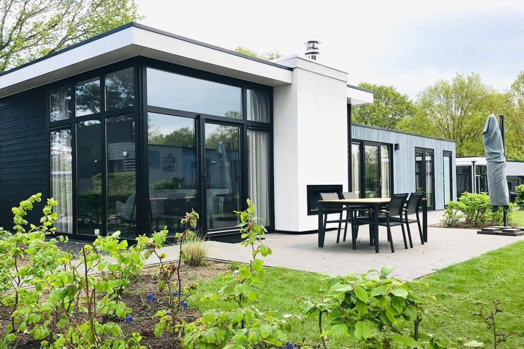 A modern house with a patio, a dining area with chairs, and a statue.