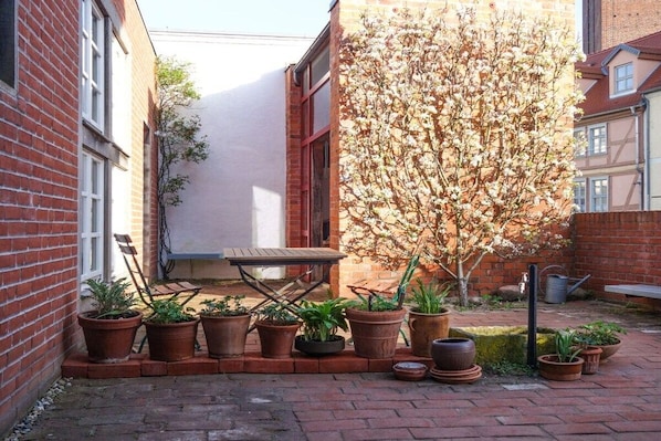 Een gebouw van baksteen met een klein terras, dat bloempotten en een houten tafel bevat.