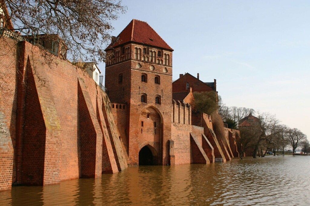 Um edifício histórico de tijolos com uma torre, parcialmente submerso em água.