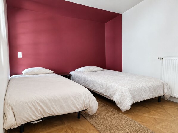 A room with two single beds, a red accent wall, a white radiator, and a wooden floor.