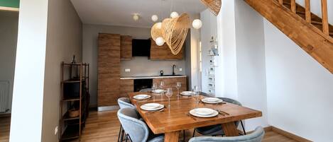 Un moderno comedor con una mesa de madera dispuesta para cuatro, sillas azul claro y una escalera con barandillas de madera.