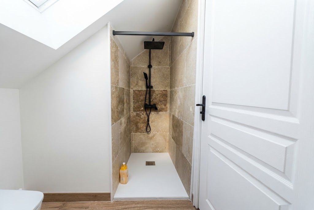 Un espace douche avec une porte blanche, une serviette et une bouteille posée sur le sol.