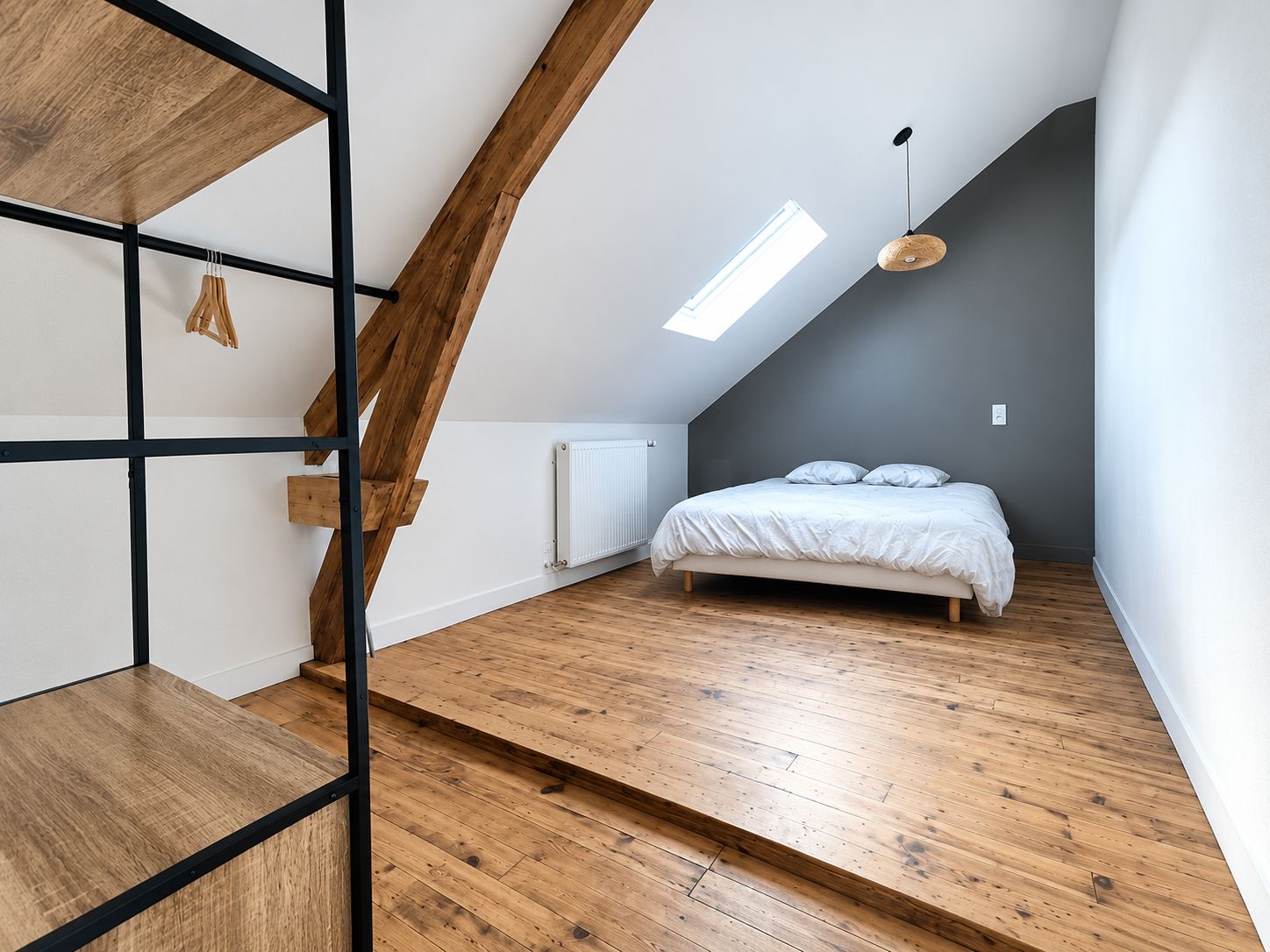 A bedroom with a sloped ceiling, a bed, a radiator, and a skylight.
