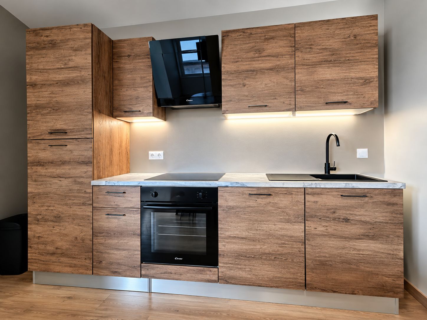Une cuisine moderne avec des meubles de rangement en bois, un four encastré et une hotte aspirante noire.