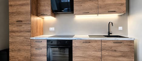 A modern kitchen with wooden cabinetry, a built-in oven, and a black range hood.