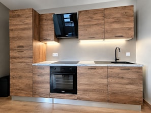 A modern kitchen with wooden cabinets, a built-in oven, and a black range hood. - Vrbo Property (Chartres)