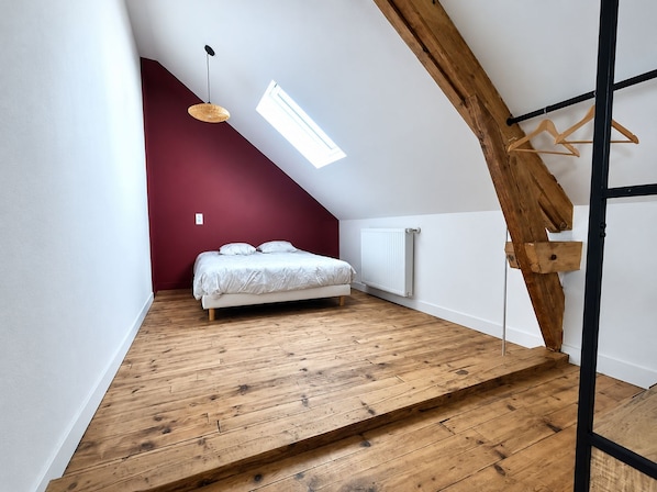 A bedroom with a sloped ceiling, a bed, a radiator, and a wooden staircase. - Vrbo Property (Chartres)