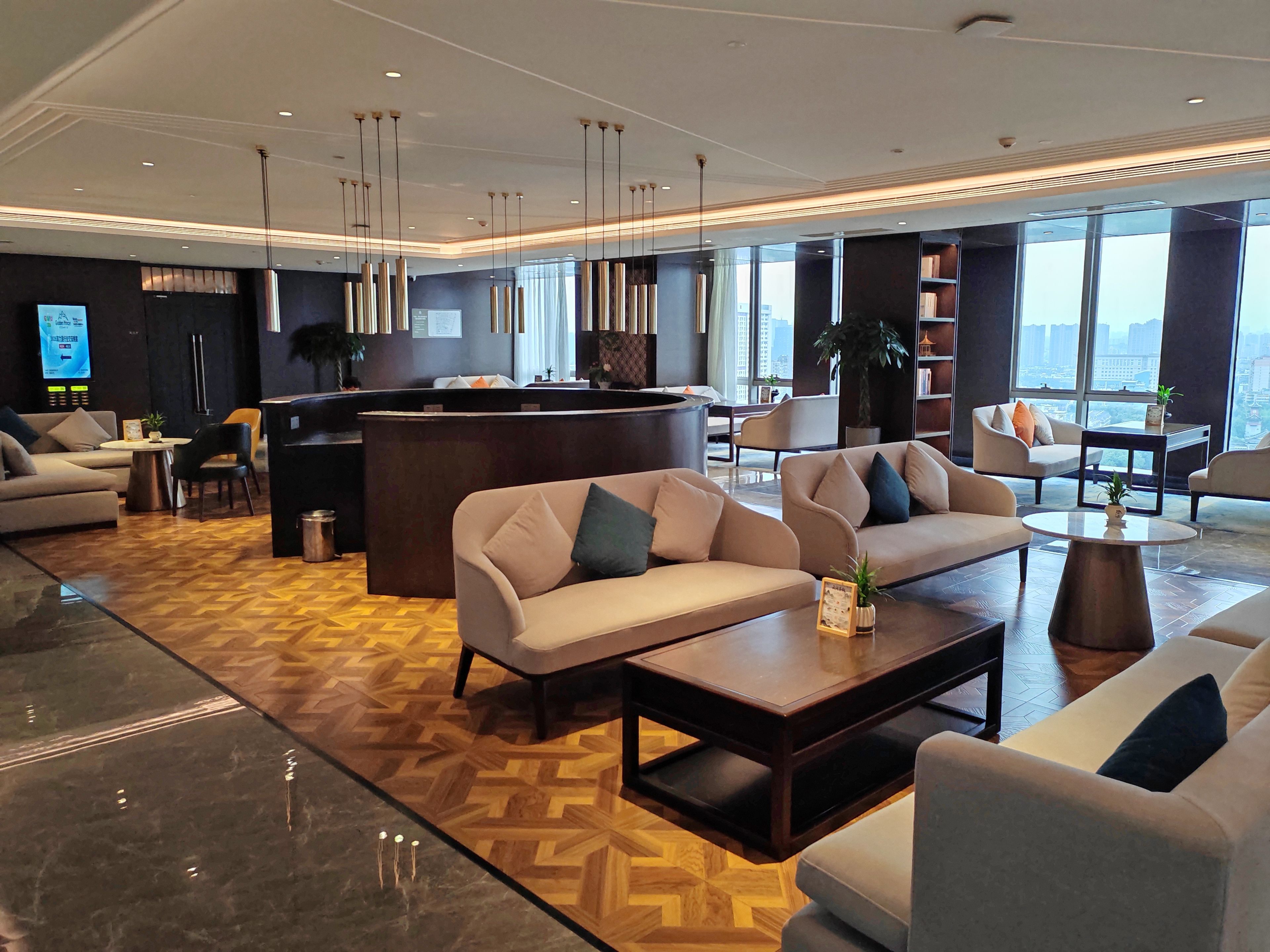 A modern hotel lobby with sofas, a reception desk, and large windows offering a city view.