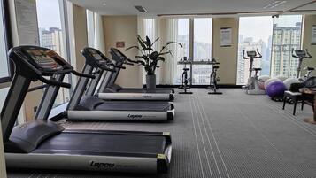 Un gimnasio con cintas de correr, bicicletas estáticas y pelotas de ejercicio, con vistas a la ciudad a través de amplios ventanales.