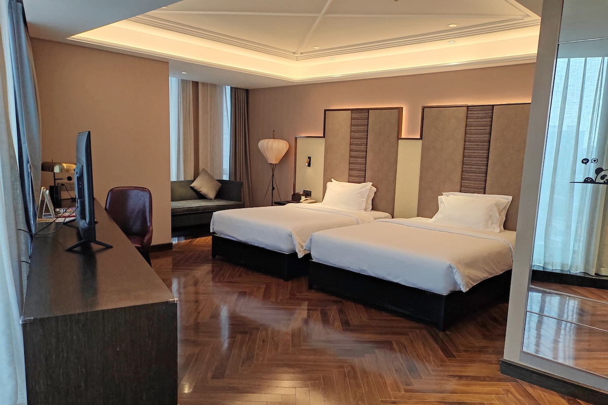 Habitación de hotel con dos camas, un escritorio con computadora, un sofá y un espejo grande.