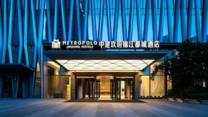 Una entrada de hotel moderna con fachada de vidrio y un cartel de Metropole Jinjiang Hotels.