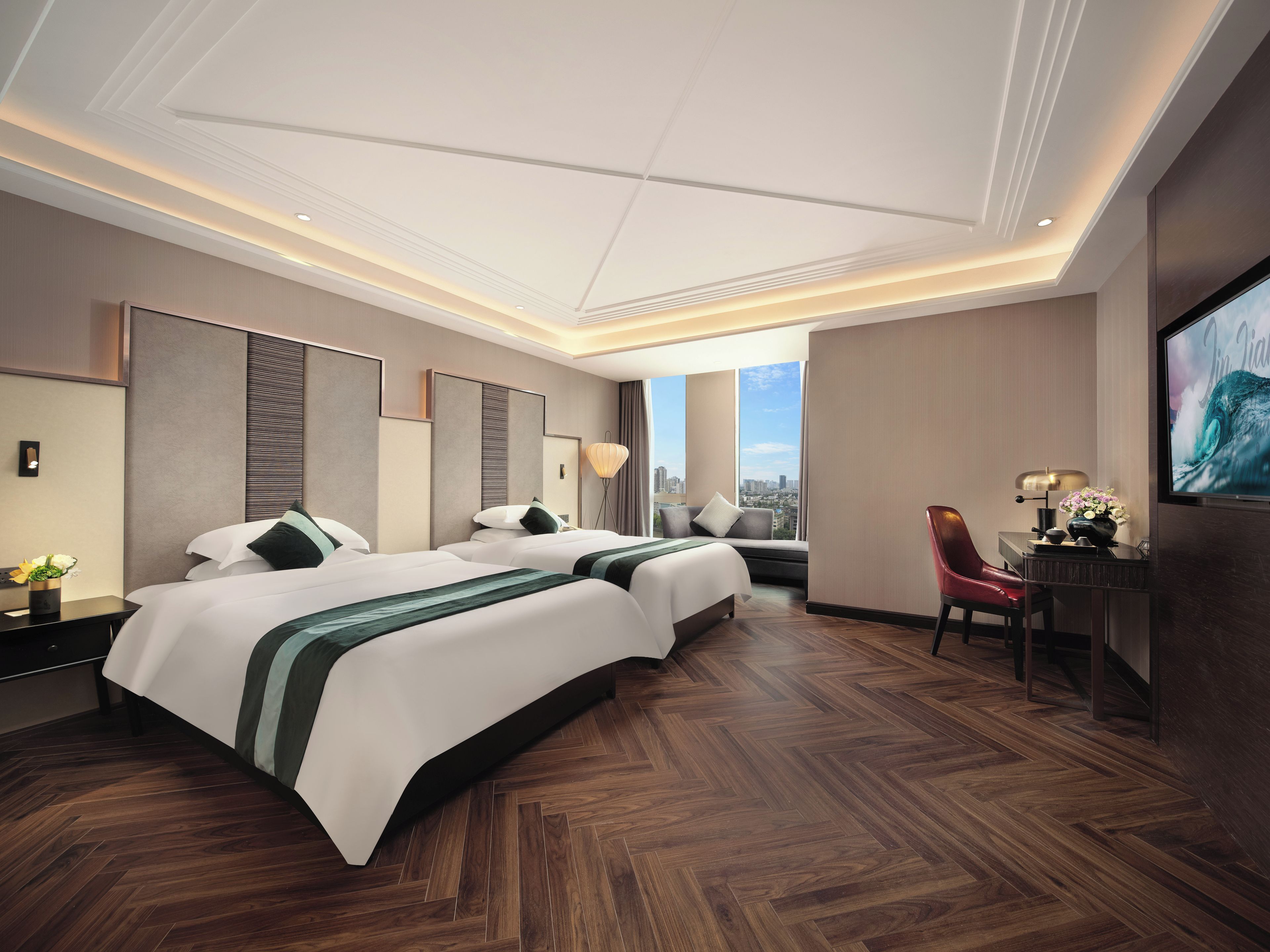 A hotel room with two beds, a desk, a chair, and a TV.