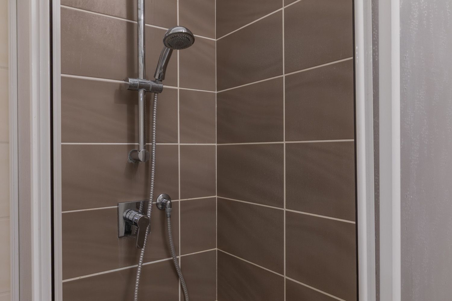 Eine Dusche mit Handbrause und einer an der Wand montierten Bedienarmatur.
