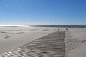 Ein hölzerner Steg führt zu einem Strand bei blauem Himmel.