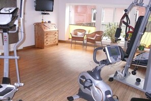 A home gym with exercise equipment, a television, and a wooden chest of drawers. - Holiday apartment with 1 bedroom (Borkum)
