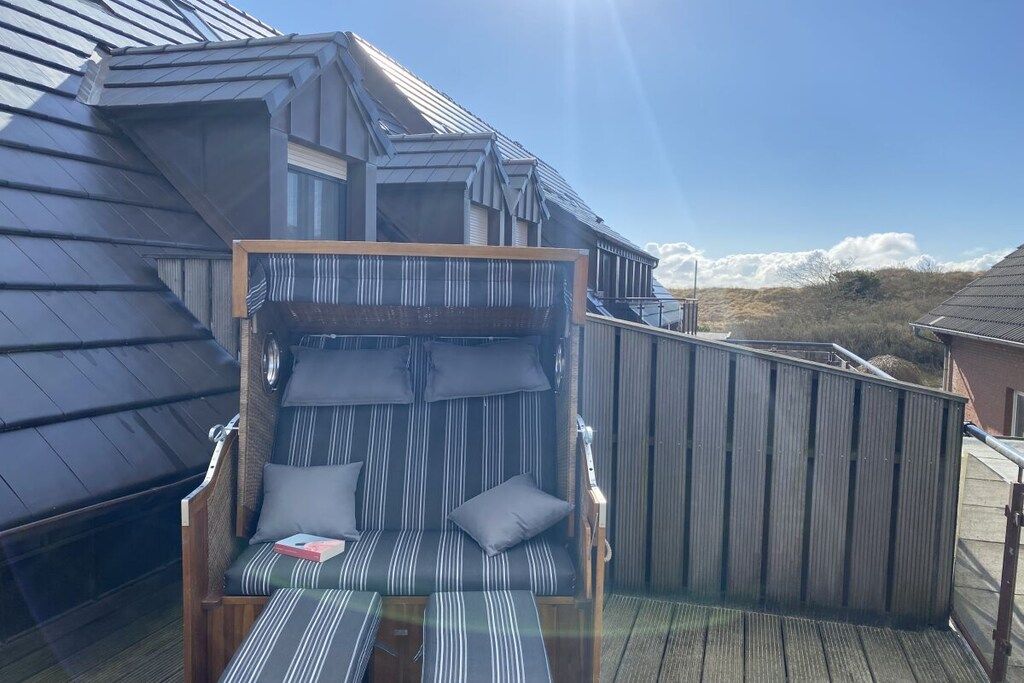 Une terrasse ensoleillée avec un coin salon confortable, une rambarde en bois et une vue sur un paysage montagneux.