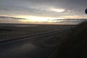 A beach with a road leading to the water, a cloudy sky, and the sun setting or rising. - Holiday apartment with 1 bedroom (Borkum)