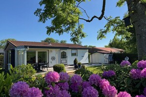 A two-story house with a covered patio, a visible door with a window, and a small garden with pink flowers. - Beach bungalow 42 Lemmer (Lemmer)