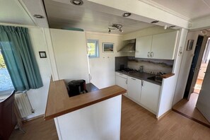 A compact kitchen with white cabinets, a wooden countertop, and a window with curtains. - Beach bungalow 42 Lemmer (Lemmer)