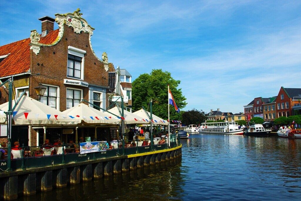 A canal-side restaurant with outdoor seating, a flag, and a boat docked nearby.