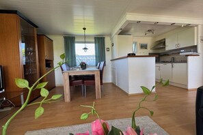A modern kitchen with white cabinets, a dining area with a wooden table, and a view of the outdoors through a window. - Beach bungalow 42 Lemmer (Lemmer)