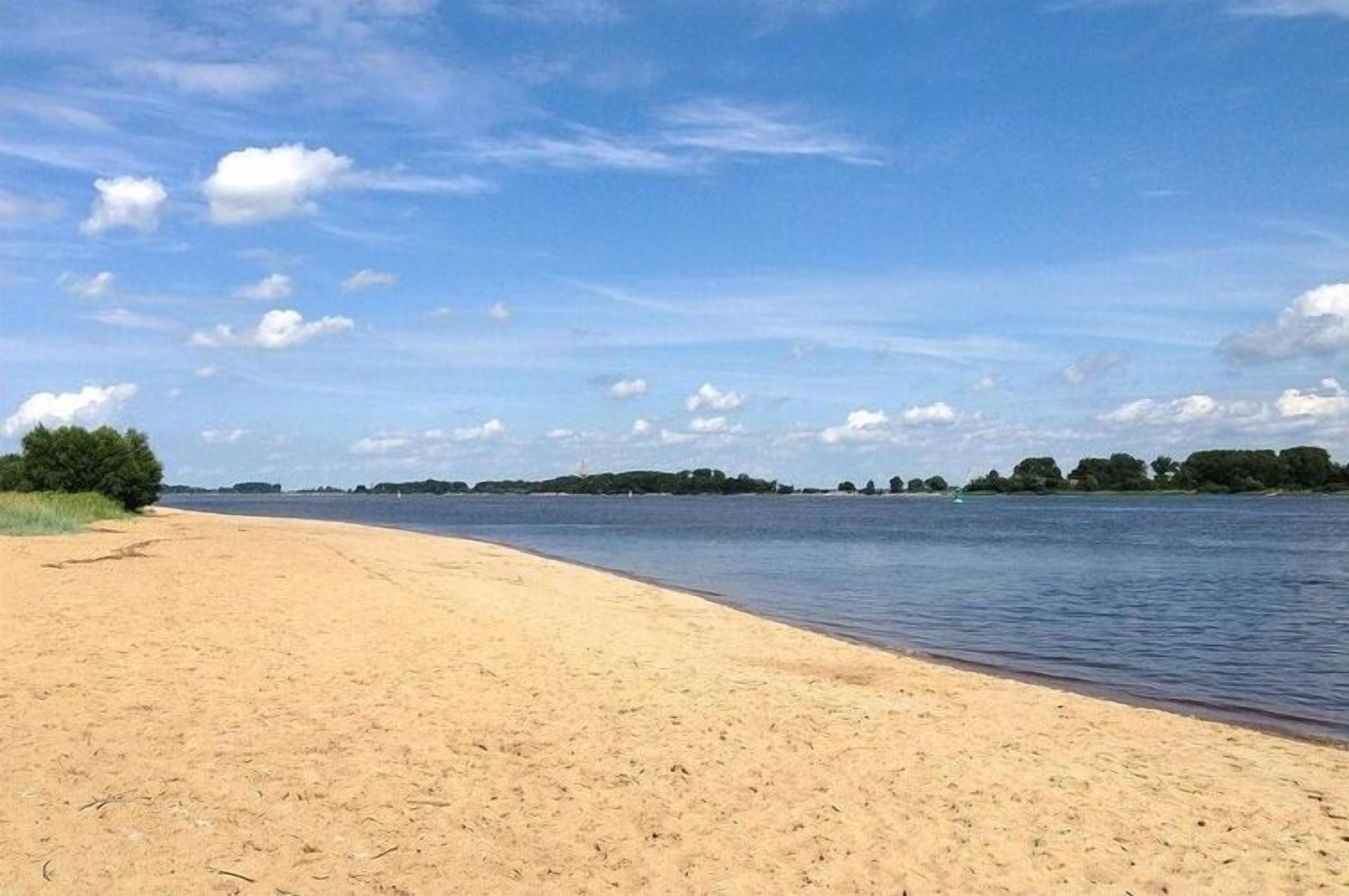 Een breed zandstrand met kalm water en een heldere lucht.