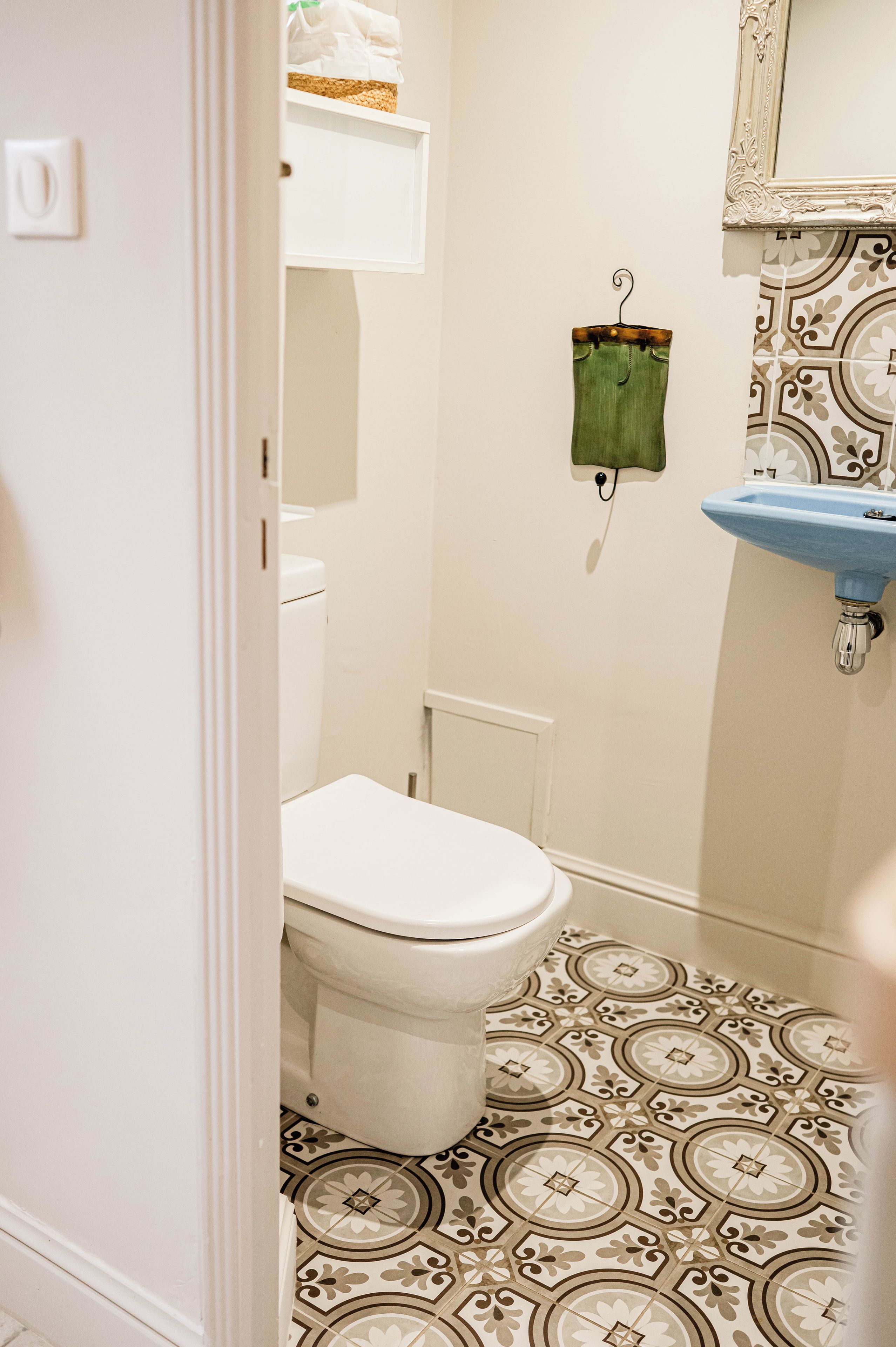 A bathroom with a toilet, a hanging green cloth, and patterned floor tiles.