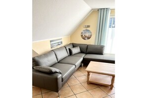 A corner living room with a sectional sofa, a small wooden table, and a wall-mounted lamp. - Holiday apartment in Lügde with swimming pool (Lügde)