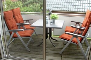 A balcony with two orange chairs and a small table, a potted plant, and a view of a building with a tiled roof. - Holiday apartment in Lügde with swimming pool (Lügde)