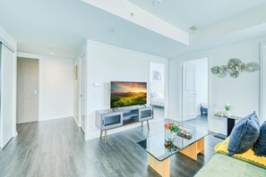 Un salon moderne avec un téléviseur à écran plat, une table basse en verre et un canapé agrémenté de coussins.