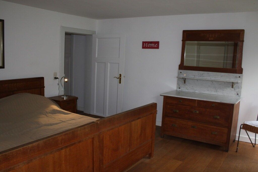 Une chambre à coucher avec un lit en bois, une commode, un miroir et une porte sur laquelle est inscrit le mot « Accueil ».